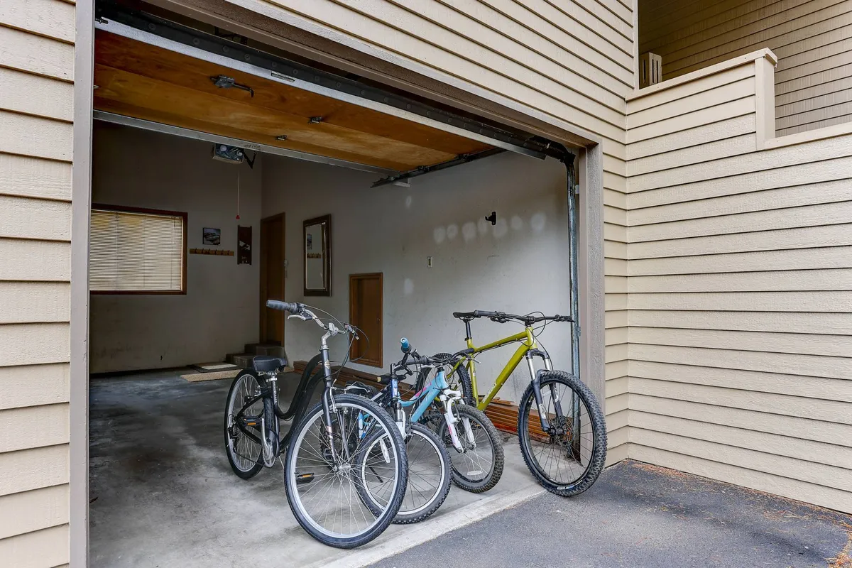 This image shows the garage interior with three bicycles, a wooden door, and practical storage space. The presence of the garage aligns with the feature of the private EV charging station, and the bikes hint at the home's access to biking paths.