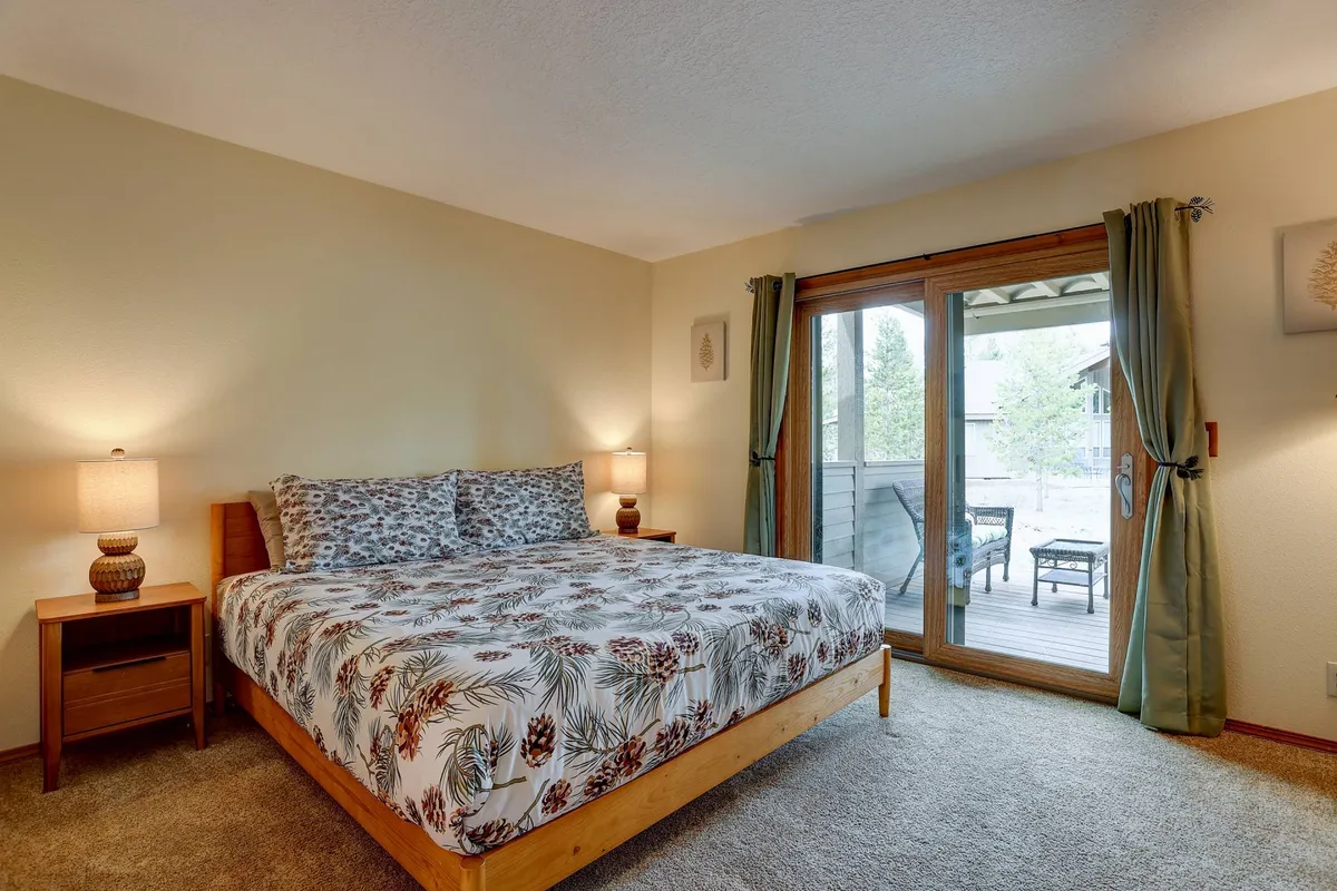 This image depicts a cozy bedroom featuring a bed with patterned bedding, a nightstand with a lamp, and a sliding glass door that opens to a balcony, inviting in natural light and offering easy outdoor access.