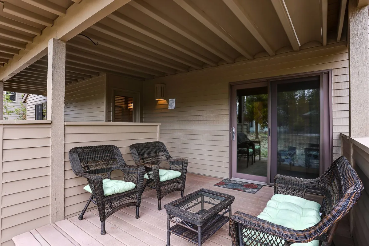 A cozy sunroom or patio area with wicker furniture and a glass coffee table sits adjacent to a sliding door, letting in abundant natural light. The inviting atmosphere hints at relaxing mornings with coffee or evenings spent together watching the sunset.