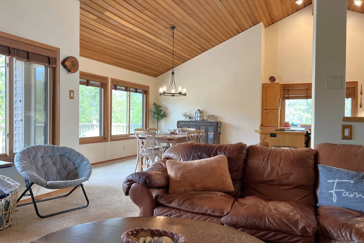 A spacious, sun-drenched interior featuring large windows with views, a comfortable leather sofa, and a stylish dining area. The scene evokes a sense of warmth, relaxation, and connection to the outdoors, with sunlight streaming in and a seamless flow between indoor comfort and natural surroundings.